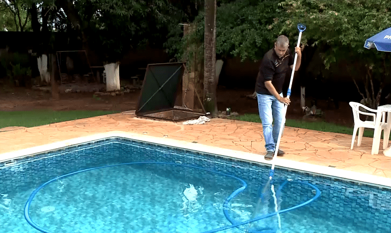 Homem limpando a piscina.