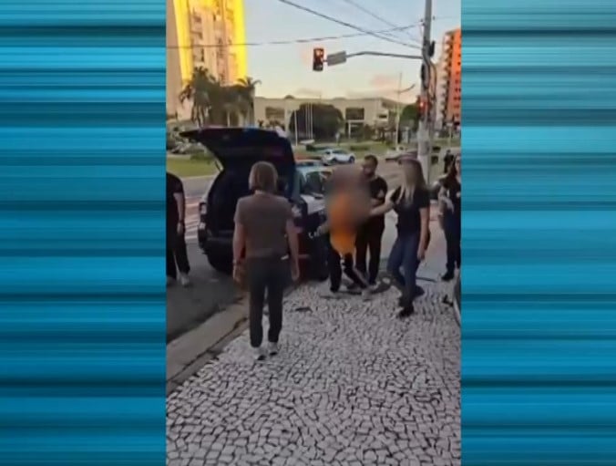 Homem sendo levado at&eacute; o carro da pol&iacute;cia.