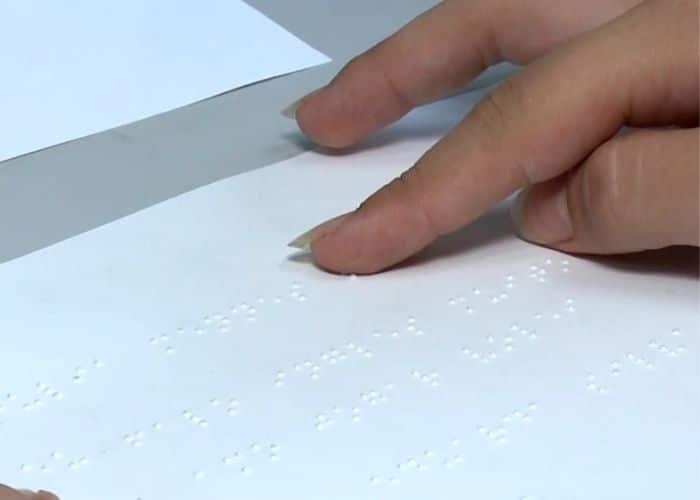 Pessoa lendo em Braille uma folha de papel.