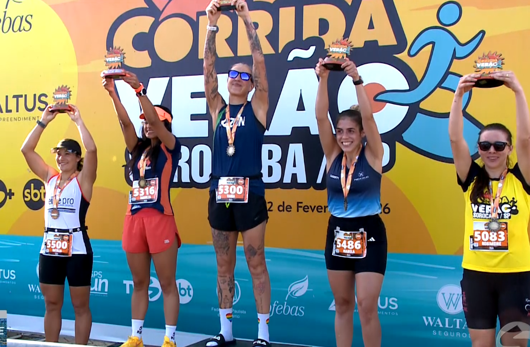 Corredoras levantando a medalha em frente ao backdrop da corrida.,