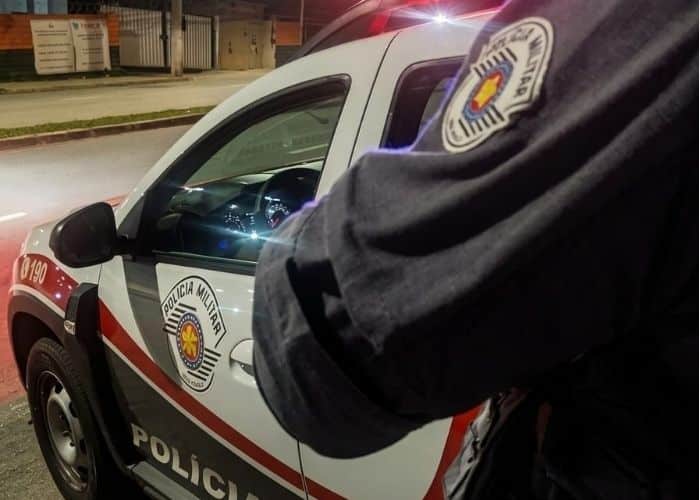 Imagem de um policial ao lado da viatura da PM
