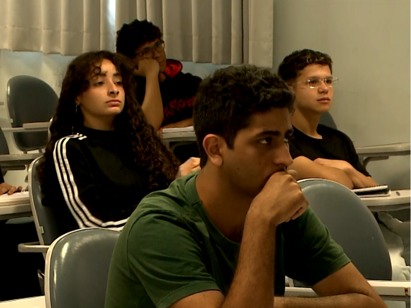 Alunos sentados em cadeiras na sala de aula prestando aten&ccedil;&atilde;o.