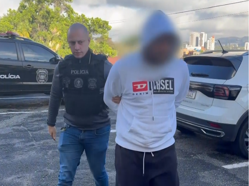 Policial levando suspeito algemado.